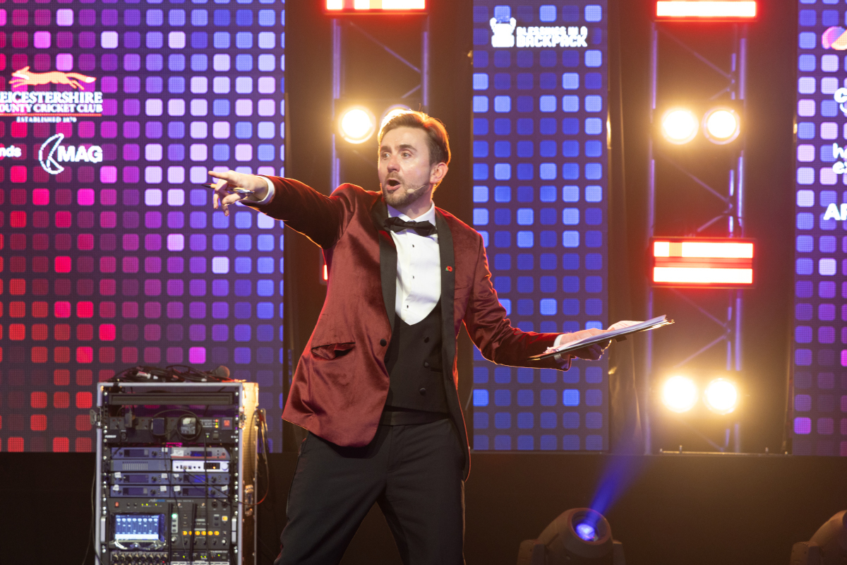 Kevin Durham auctioneering on stage in a red velvet jacket under dramatic red and blue lighting Kevin Durham auctioneering on stage in a red velvet jacket under dramatic red and blue lighting