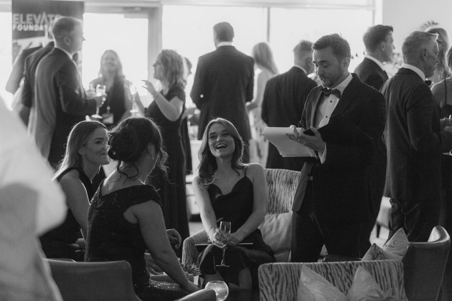 Black and white photo of guests mingling at a charity gala while the auctioneer works the room Black and white photo of guests mingling at a charity gala while the auctioneer works the room