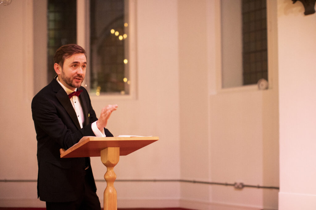 Charity auctioneer in black tie speaking from a wooden lectern at a fundraising dinner Charity auctioneer in black tie speaking from a wooden lectern at a fundraising dinner
