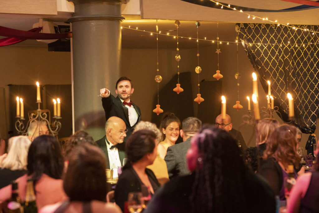 Charity auctioneer taking a bid from the floor among guests at a candlelit gala Charity auctioneer taking a bid from the floor among guests at a candlelit gala