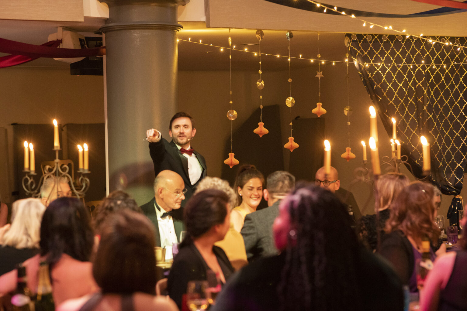 Charity auctioneer taking a bid from the floor among guests at a candlelit gala