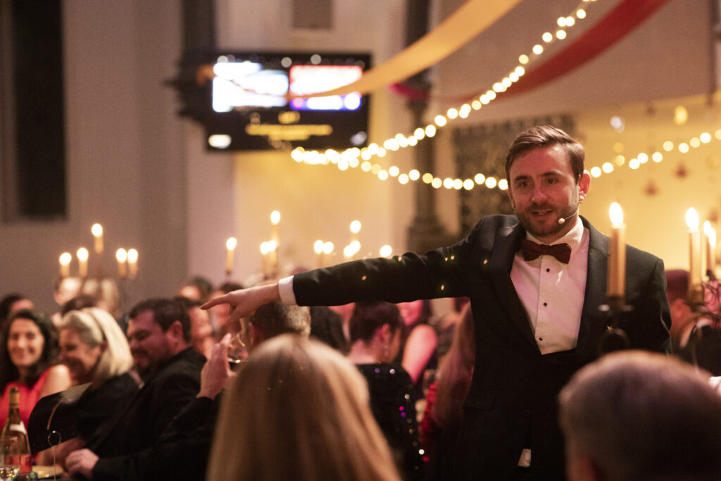 Charity auctioneer in a black dinner jacket pointing to a bidder at a candlelit gala dinner Charity auctioneer in a black dinner jacket pointing to a bidder at a candlelit gala dinner