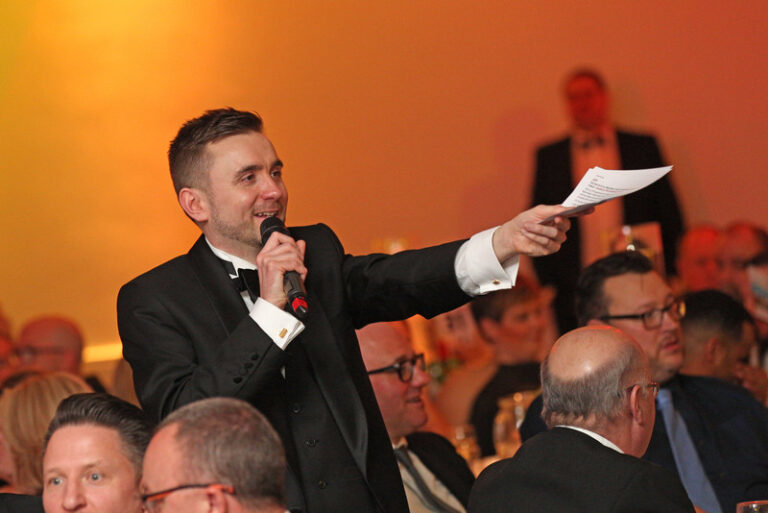 Auctioneer in black tie taking bids among seated guests at a gala dinner Auctioneer in black tie taking bids among seated guests at a gala dinner