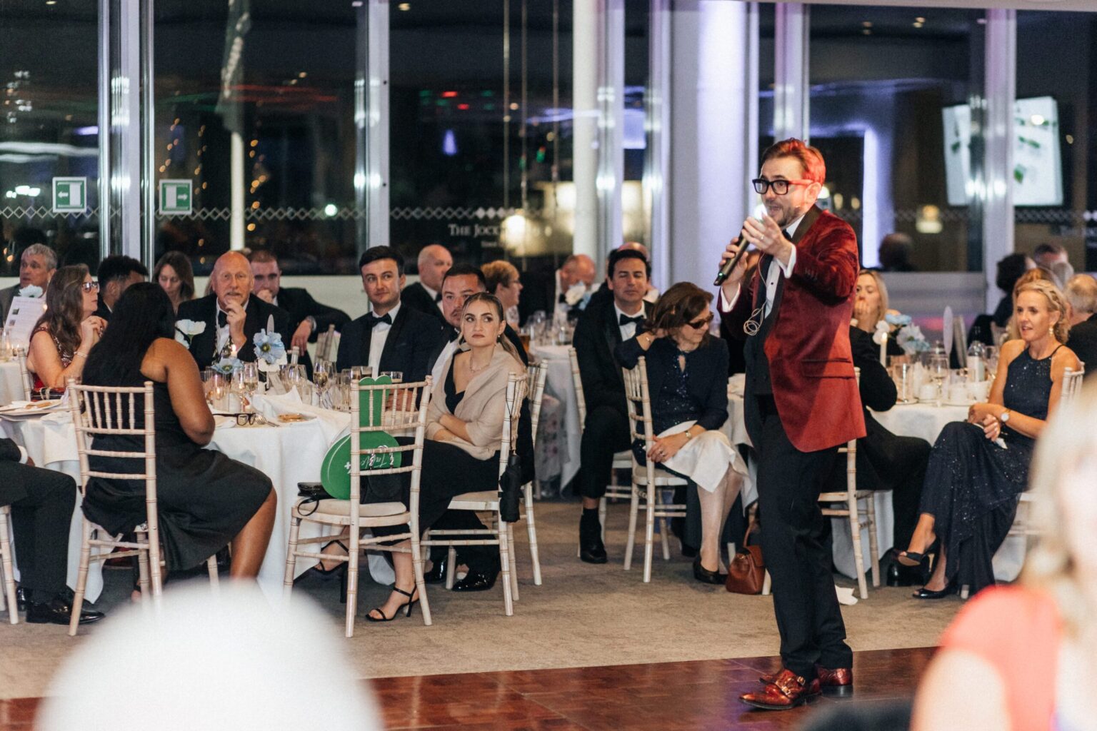 Charity auctioneer Kevin Durham running the live auction at Jigsaw Trust's charity gala, addressing guests with a wireless microphone from the floor.