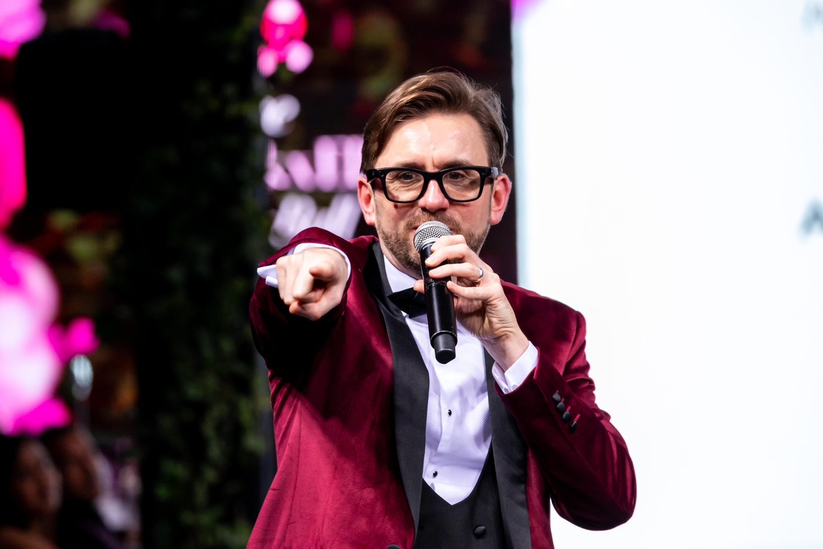 Kevin Durham in a burgundy velvet dinner jacket working a room on the microphone as event host